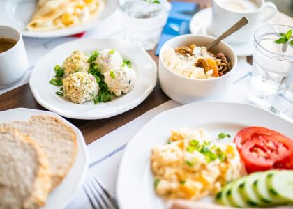 From above of tasty brunch of power bowl and scrambled eggs with fresh vegetable slices against drinks on table